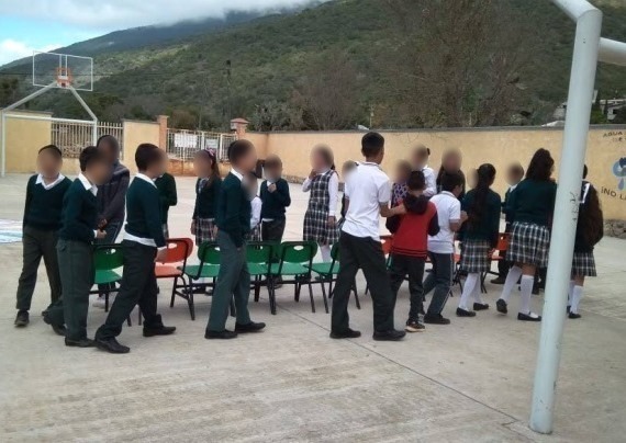 Se muestra un grupo de niños cerca de una hilera de sillas, caminando. Realizando la actividad Al Son Que Me Toques