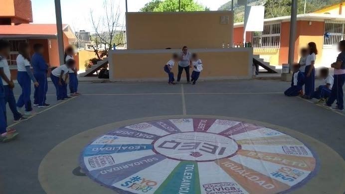 Se muestra un grupo de niños cerca de un circulo que contiene valores como: legalidad, respeto, igualdad. Al fondo dos niños se preparan para correr. Corre por Ciro